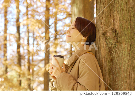 Middle-aged woman drinking coffee among autumn leaves Middle-aged woman drinking coffee among autumn leaves 129809843