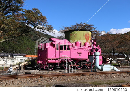 A bright pink steam locomotive against a blue sky and white clouds 129810330
