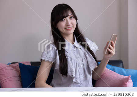 A smiling Japanese woman holding a smartphone in the living room A smiling Japanese woman holding a smartphone in the living room 129810368