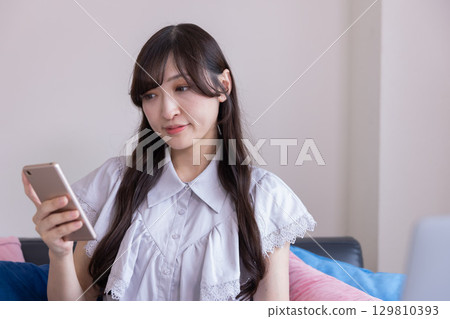 客廳裡，一位面帶微笑的日本女性手裡拿著智慧型手機 129810393
