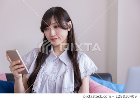 客廳裡，一位面帶微笑的日本女性手裡拿著智慧型手機 129810409