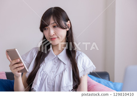 客廳裡，一位面帶微笑的日本女性手裡拿著智慧型手機 129810410