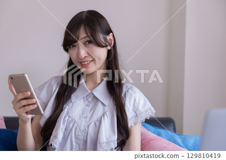 A smiling Japanese woman holding a smartphone in the living room A smiling Japanese woman holding a smartphone in the living room 129810419
