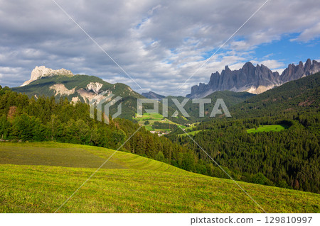 Stone mountain peaks and green nature of Val di Funes, Dolomites with settlements in background Stone mountain peaks and green nature of Val di Funes, Dolomites with settlements in background 129810997