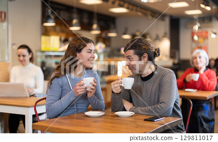 Couple are chatting happily with each other while sitting at table in cafe and drinking tea Couple are chatting happily with each other while sitting at table in cafe and drinking tea 129811017