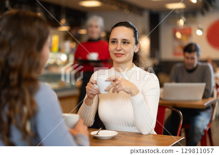Woman in cafe sits opposite female companion, has nice conversation 129811057