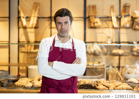 Confident baker in maroon apron posing with arms crossed 129811101