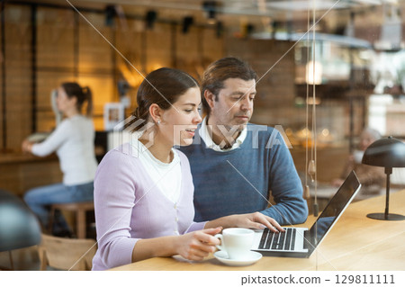 Man and woman looking at laptop screen while having lunch at bar counter of cafe 129811111