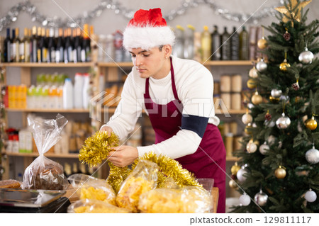 Guy employee decorates trading floor of minimarket by tinsel at New Year Eve 129811117