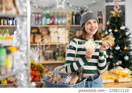 Feale customer with cart of groceries buys tasty cheese in supermarket - prepares to celebrate Christmas 129811118
