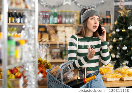 Woman talking on her mobile phone - asking for advice on what products to buy at supermarket for Christmas 129811138