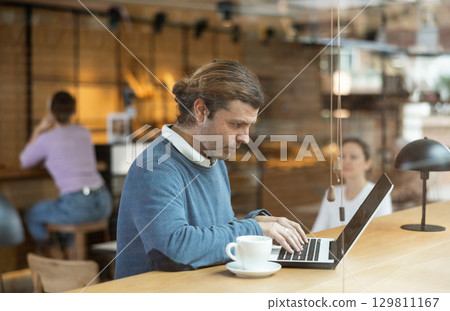 Man using laptop and drinking coffee in modern cafe Man using laptop and drinking coffee in modern cafe 129811167