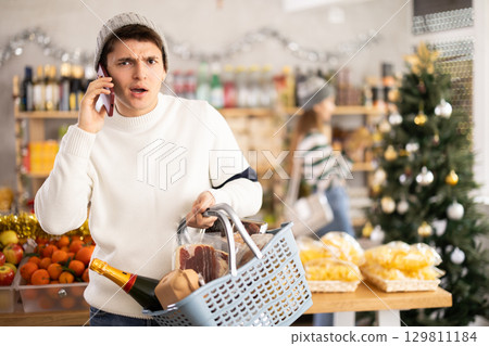 Guy talking on her mobile phone - asking for advice on what products to buy at supermarket for Christmas 129811184