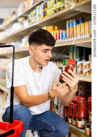 Guy reading label on bottle with tomato juice in supermarket 129811189