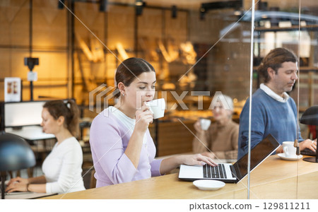 Confident female cafe customer enjoying peace and quiet while working on laptop 129811211