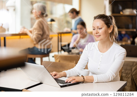 Woman spending time in cozy coffeehouse with laptop and coffee Woman spending time in cozy coffeehouse with laptop and coffee 129811284