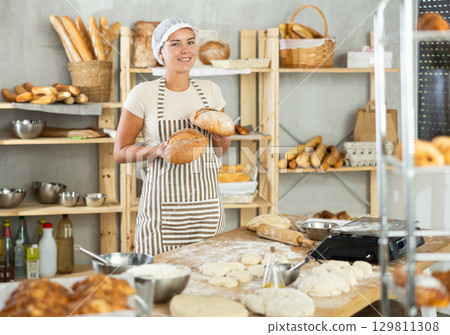 Young woman are standing in kitchen with finished products two loaves of rye bread Young woman are standing in kitchen with finished products two loaves of rye bread 129811308