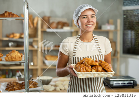 Smiling young female baker offering freshly baked croissants 129811319