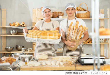 Two smiling young bakers holding freshly baked goods in bakery 129811337