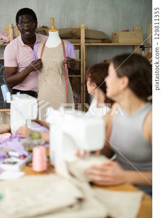 Sewing school African man teacher conducts lesson for students using mannequin 129811355