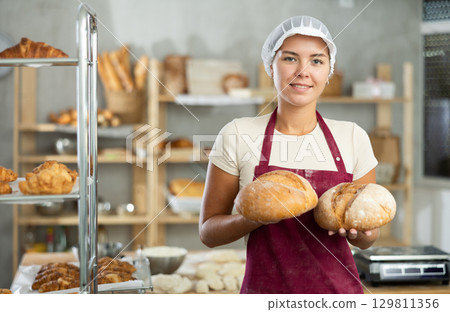 Young woman are standing in kitchen with finished products two loaves of rye bread 129811356
