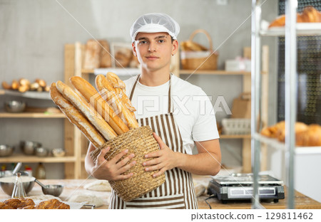 Happy male baker posing with basket of freshly baked baguettes in bakery, demonstrating concept of food industry and baker profession 129811462