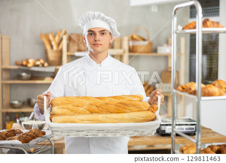 Happy male baker posing with basket of freshly baked baguettes in bakery, demonstrating concept of food industry and baker profession Happy male baker posing with basket of freshly baked baguettes in bakery, demonstrating concept of food industry and baker profession 129811463