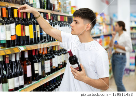 Interested young guy choosing alcoholic beverages in store Interested young guy choosing alcoholic beverages in store 129811488