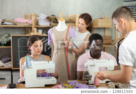 Woman and African man sewing, other student create paper dress pattern, work with mannequin Woman and African man sewing, other student create paper dress pattern, work with mannequin 129811583