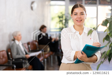 Friendly girl with folder of documents stands in office 129811621