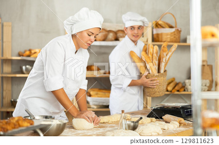 Working in bakery - woman kneads raw dough to make baguettes or croissants 129811623