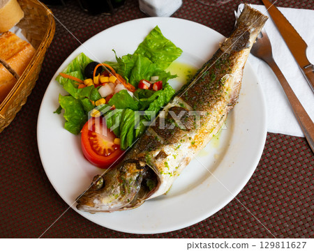 There is plate with fried whole carcass zander fish and mix vegetable salad on table There is plate with fried whole carcass zander fish and mix vegetable salad on table 129811627