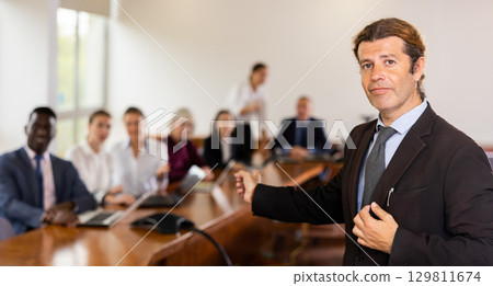 Gentle mid-aged white brunette businessman posing with welcoming hand gesture Gentle mid-aged white brunette businessman posing with welcoming hand gesture 129811674