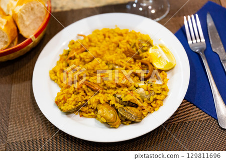 Portion of freshly prepared crumbly paella with seafood, supplemented with lemon 129811696