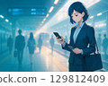 早上，一位穿著西裝的女士在火車站台上查看她的智慧型手機和通勤卡 129812409