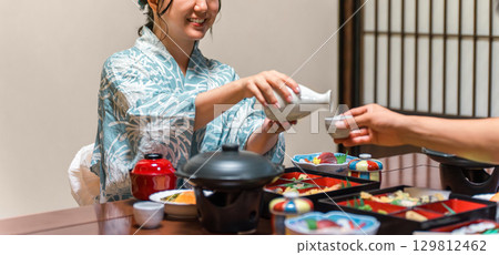 Young Asian woman in yukata serving drinks at dinner in a ryokan, couple, husband and wife 129812462