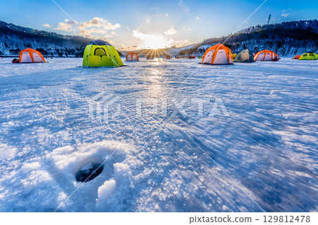 Colorful smelt fishing tents on the ice of a frozen lake and the cold early morning sun in sub-zero temperatures Colorful smelt fishing tents on the ice of a frozen lake and the cold early morning sun in sub-zero temperatures 129812478