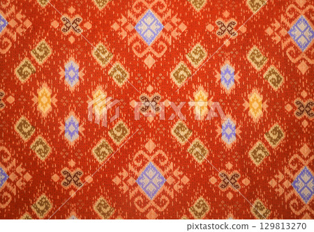Traditional Indonesian batik cloth with elegant hand-drawn motifs in orange 129813270