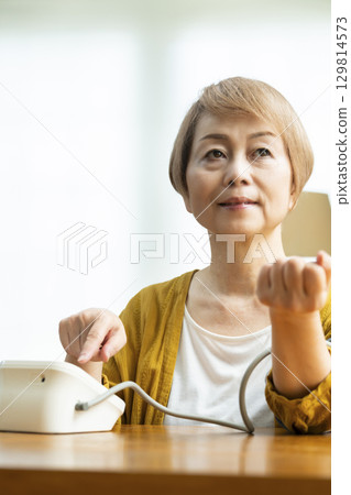 一位老年婦女在客廳測量血壓 一位老年婦女在客廳測量血壓 129814573