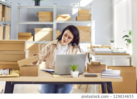 Woman working in warehouse checking stock and inventory sitting at the desk on workplace Woman working in warehouse checking stock and inventory sitting at the desk on workplace 129814655