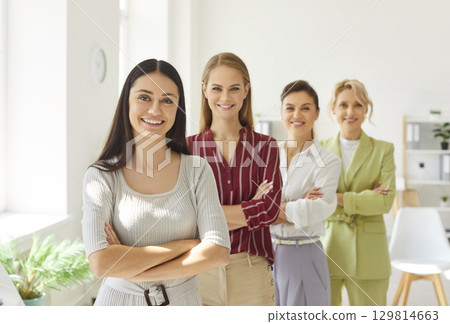 Happy young business women group in casual clothes standing in office and looking at camera Happy young business women group in casual clothes standing in office and looking at camera 129814663