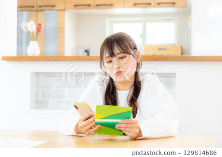 A woman looking at her smartphone and bankbook 129814686