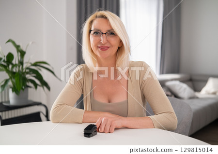 Relaxed blonde lady sitting in modern living room using pulse oximeter to monitor heart rate and smiling Relaxed blonde lady sitting in modern living room using pulse oximeter to monitor heart rate and smiling 129815014