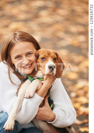 Sitting, holding animal and looking into the camera. Young woman is with her dog in the park Sitting, holding animal and looking into the camera. Young woman is with her dog in the park 129816732