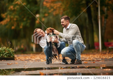 Autumn season walk. Lovely couple are with their cute dog outdoors 129816815