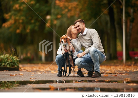 Autumn season walk. Lovely couple are with their cute dog outdoors 129816816