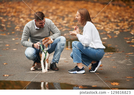 Sitting, playing with animal. Lovely couple are with their cute dog outdoors Sitting, playing with animal. Lovely couple are with their cute dog outdoors 129816823