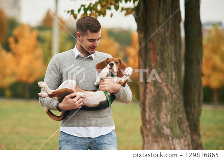 Young man is standing in the park and holding his cocker spaniel dog in hands 129816865