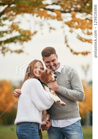Smiling, having fun. Lovely couple are with their cute dog outdoors 129816866