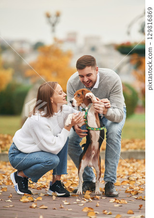 Holding animal by the legs, making him stand straight. Lovely couple are with their cute dog outdoors Holding animal by the legs, making him stand straight. Lovely couple are with their cute dog outdoors 129816869